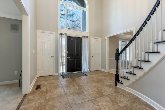 entrance foyer with visible vents, baseboards, stairs, light tile patterned floors, and a high ceiling