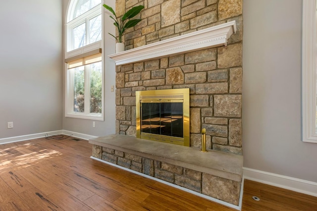 unfurnished living room featuring a stone fireplace, baseboards, and hardwood / wood-style floors