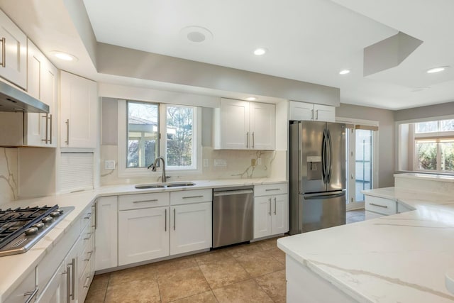 kitchen with a sink, white cabinetry, appliances with stainless steel finishes, decorative backsplash, and light stone countertops