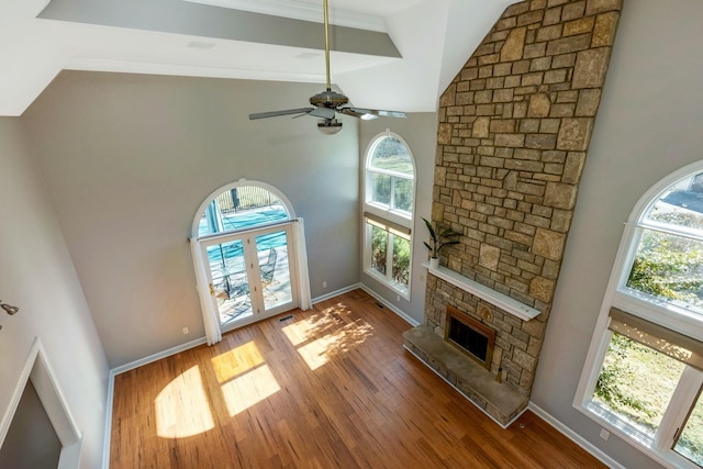 living room featuring a ceiling fan, wood finished floors, a high ceiling, a fireplace, and baseboards