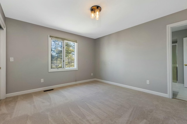 empty room featuring baseboards, visible vents, and light carpet