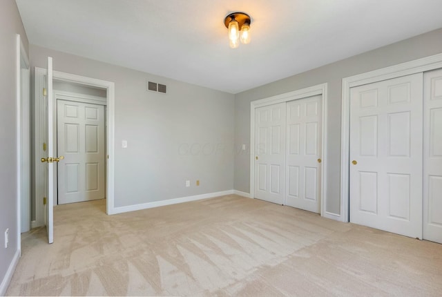 unfurnished bedroom with visible vents, light carpet, two closets, and baseboards