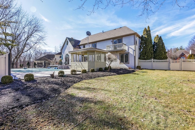 back of house featuring stucco siding, fence, a yard, a fenced in pool, and a balcony