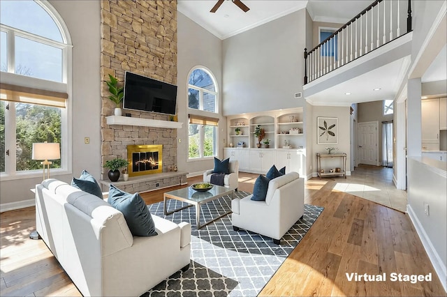 living area featuring baseboards, a stone fireplace, wood finished floors, and crown molding