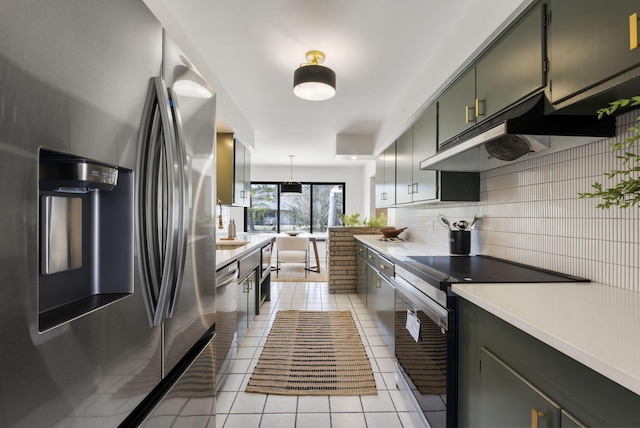 kitchen with light tile patterned floors, tasteful backsplash, light countertops, appliances with stainless steel finishes, and under cabinet range hood