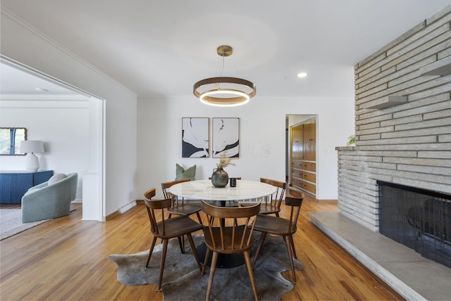 dining space featuring a large fireplace, baseboards, wood finished floors, and crown molding