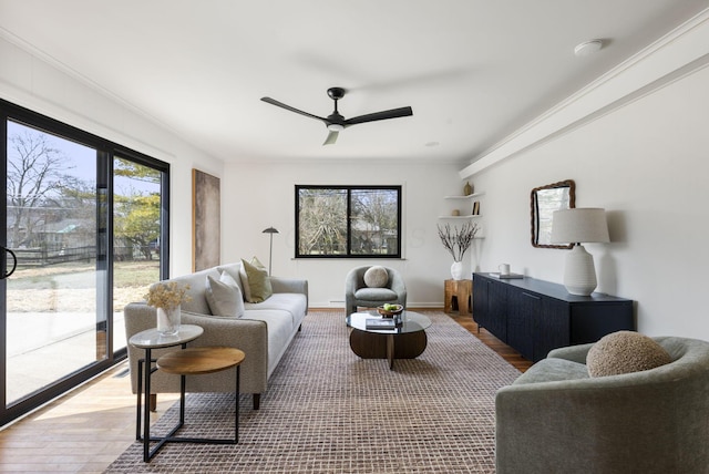 living area with baseboards, crown molding, a ceiling fan, and wood finished floors