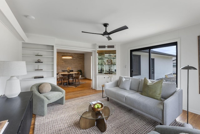 living room with built in shelves, wood finished floors, and a ceiling fan