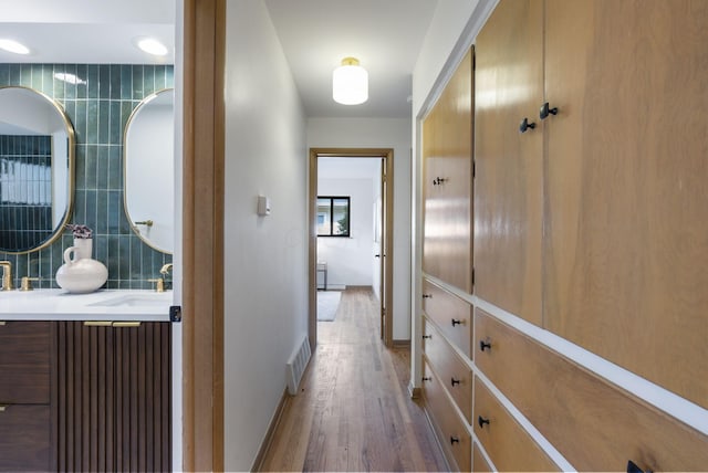 hall with tile walls, visible vents, light wood-style flooring, a sink, and baseboards