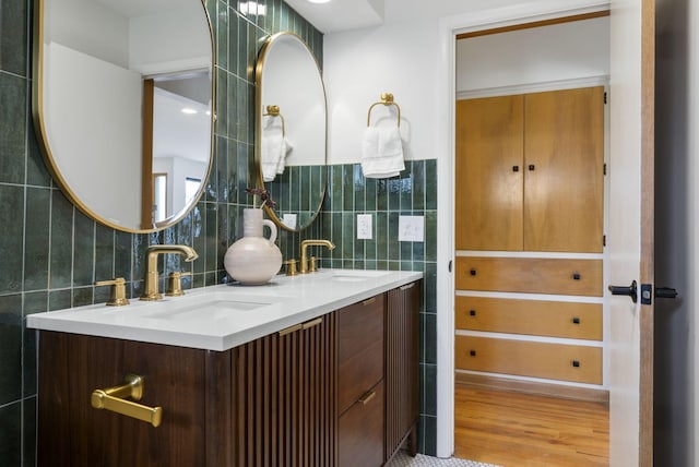 full bathroom featuring double vanity, tile walls, a sink, and wood finished floors