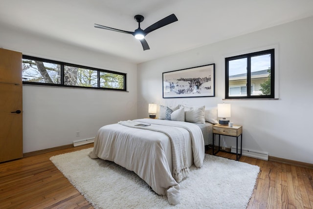 bedroom with a baseboard heating unit, multiple windows, baseboard heating, and hardwood / wood-style flooring