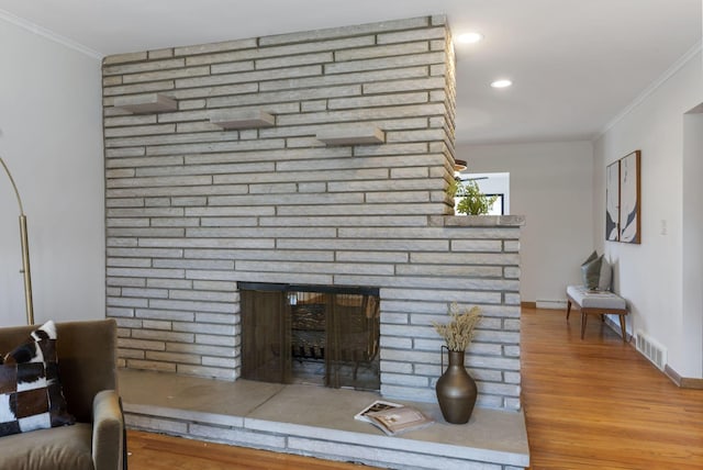 living area with ornamental molding, a brick fireplace, wood finished floors, and visible vents