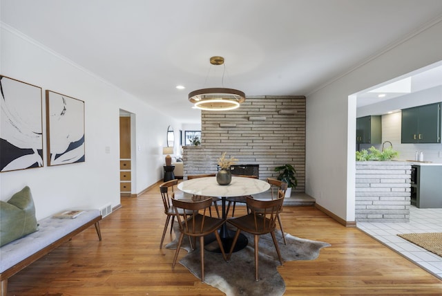 dining area with a fireplace, light wood finished floors, recessed lighting, ornamental molding, and baseboards