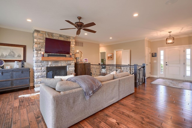 living area with baseboards, hardwood / wood-style floors, crown molding, a stone fireplace, and recessed lighting