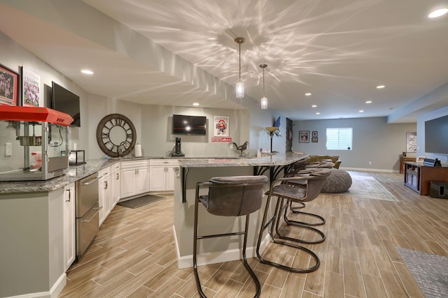kitchen with light stone counters, wood finish floors, open floor plan, white cabinetry, and a kitchen bar