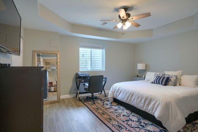 bedroom featuring baseboards, visible vents, ceiling fan, a tray ceiling, and light wood-style floors