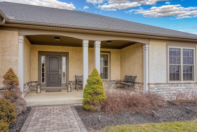 property entrance featuring stone siding, a porch, roof with shingles, and stucco siding