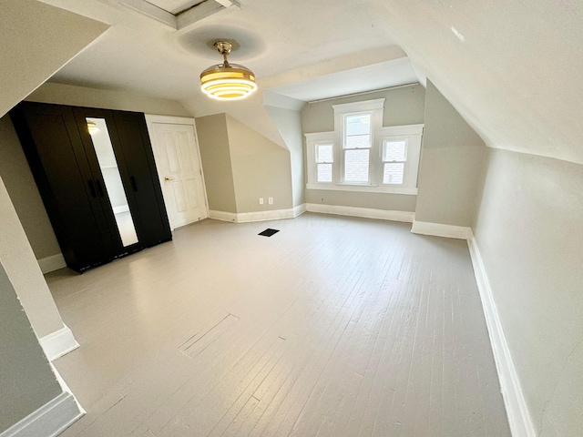 additional living space featuring light wood finished floors, baseboards, and vaulted ceiling