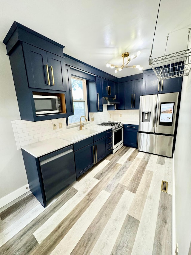 kitchen with appliances with stainless steel finishes, light countertops, light wood-type flooring, blue cabinetry, and backsplash