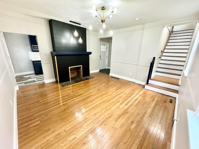 unfurnished living room with stairs, a fireplace, hardwood / wood-style flooring, and baseboards