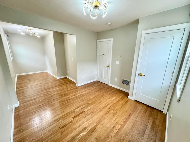 empty room featuring light wood-type flooring, an inviting chandelier, visible vents, and baseboards