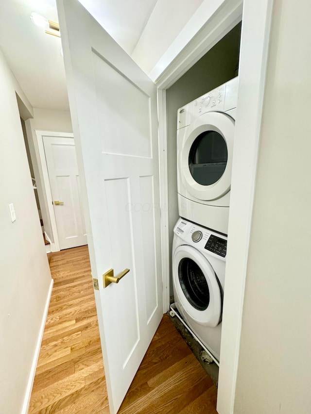 laundry room with light wood finished floors, baseboards, laundry area, and stacked washer / dryer