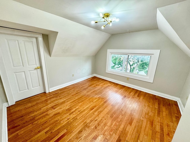 additional living space featuring lofted ceiling, light wood-style flooring, baseboards, and a notable chandelier