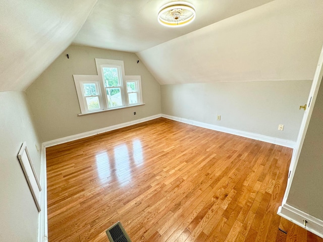 bonus room with light wood-type flooring, visible vents, baseboards, and vaulted ceiling