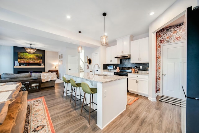 kitchen featuring white cabinets, light wood-style floors, light stone counters, a kitchen breakfast bar, and under cabinet range hood