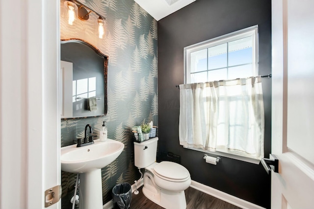 half bath featuring toilet, wallpapered walls, baseboards, and a wealth of natural light