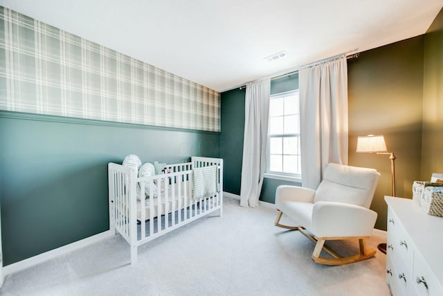 bedroom with wallpapered walls, visible vents, wainscoting, carpet, and a nursery area