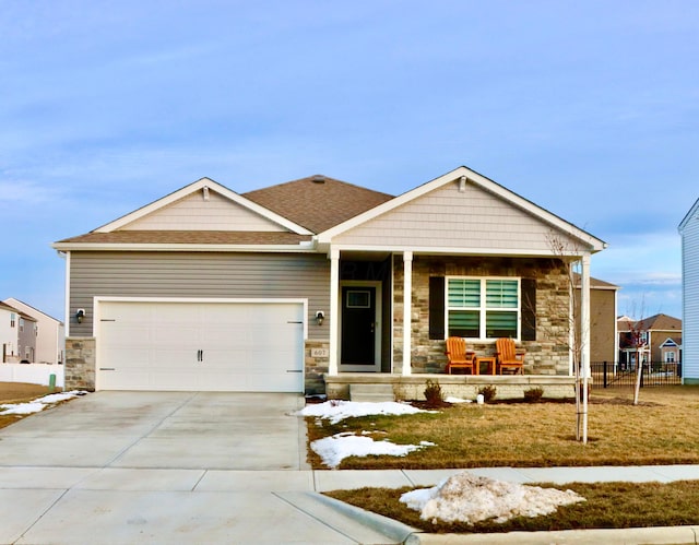 view of front of property with concrete driveway, stone siding, an attached garage, fence, and a porch