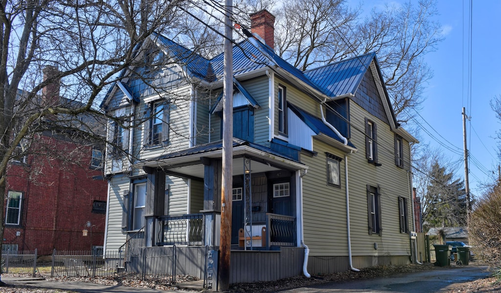 view of front of property with metal roof, a porch, a fenced front yard, and a chimney