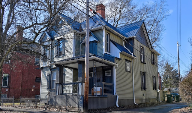 view of front of property with metal roof, a porch, a fenced front yard, and a chimney