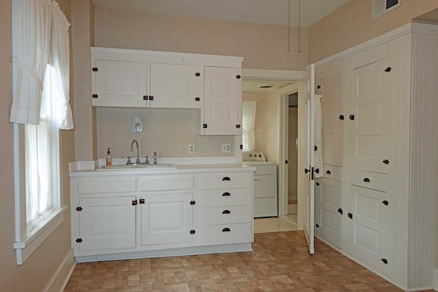 kitchen with a sink, visible vents, white cabinetry, light countertops, and washer / dryer