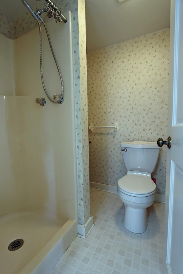 bathroom with a stall shower, baseboards, toilet, and wallpapered walls