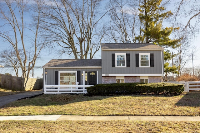 split level home featuring brick siding, board and batten siding, a front lawn, and fence