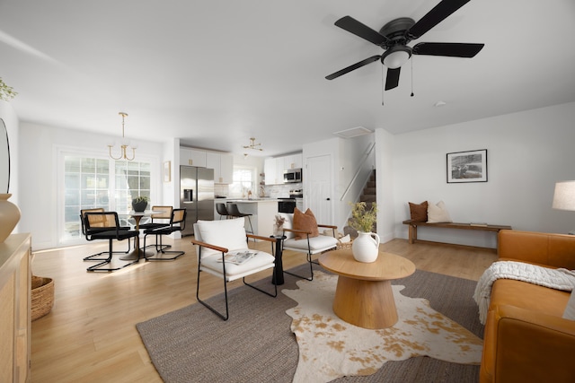 living area featuring ceiling fan with notable chandelier, stairway, and light wood-style floors