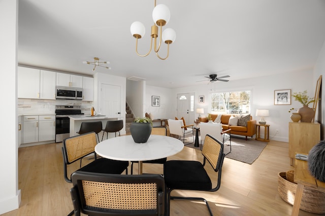 dining space with ceiling fan with notable chandelier, stairway, baseboards, and light wood-style floors