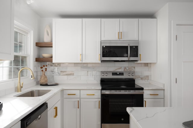 kitchen featuring stainless steel appliances, a sink, white cabinetry, open shelves, and tasteful backsplash