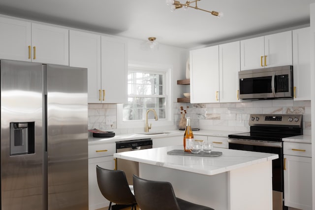 kitchen featuring stainless steel appliances, a sink, white cabinetry, a kitchen breakfast bar, and tasteful backsplash