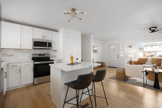 kitchen with appliances with stainless steel finishes, open floor plan, a center island, a kitchen bar, and backsplash