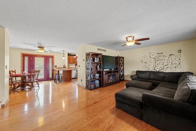 living room with light wood-style floors, visible vents, ceiling fan, and a lit fireplace