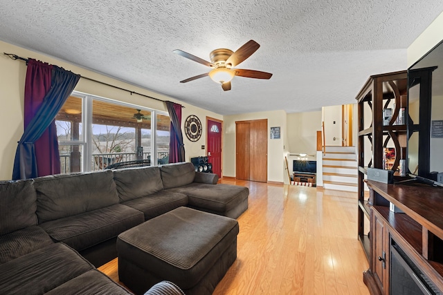 living area with light wood-style floors, stairway, a textured ceiling, and a ceiling fan