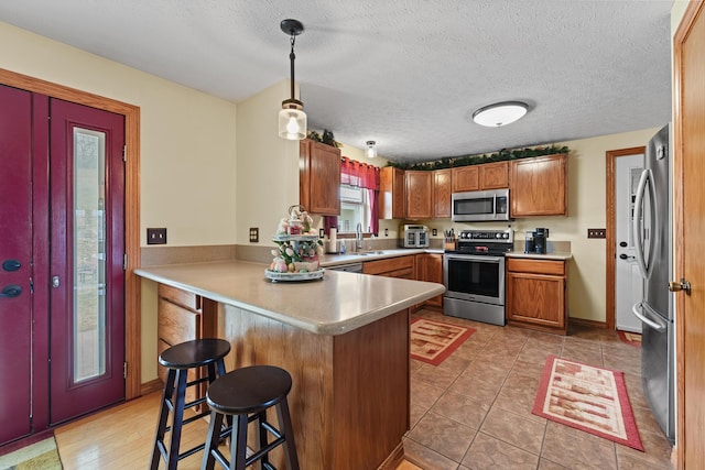 kitchen with a peninsula, light countertops, appliances with stainless steel finishes, brown cabinetry, and a kitchen bar