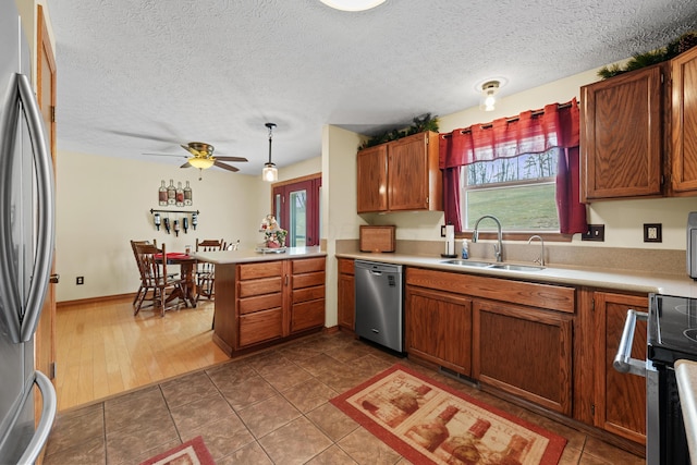 kitchen featuring brown cabinets, a peninsula, stainless steel appliances, light countertops, and a sink