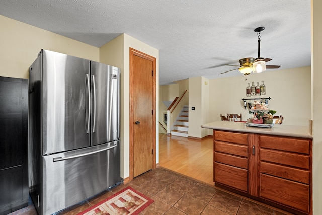 kitchen featuring a textured ceiling, dark tile patterned floors, a ceiling fan, freestanding refrigerator, and brown cabinetry