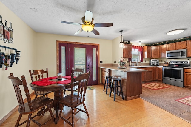 dining area featuring ceiling fan, a textured ceiling, light wood-type flooring, and baseboards