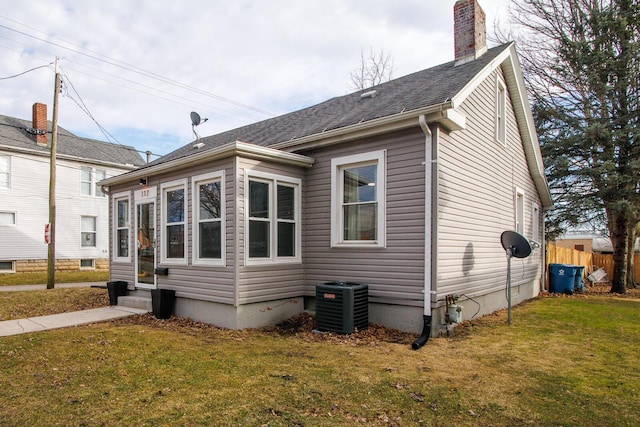 view of home's exterior featuring a chimney, a lawn, entry steps, central AC, and fence