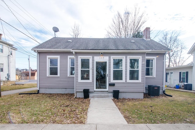 view of front of home with a shingled roof, a front yard, central AC, and a chimney